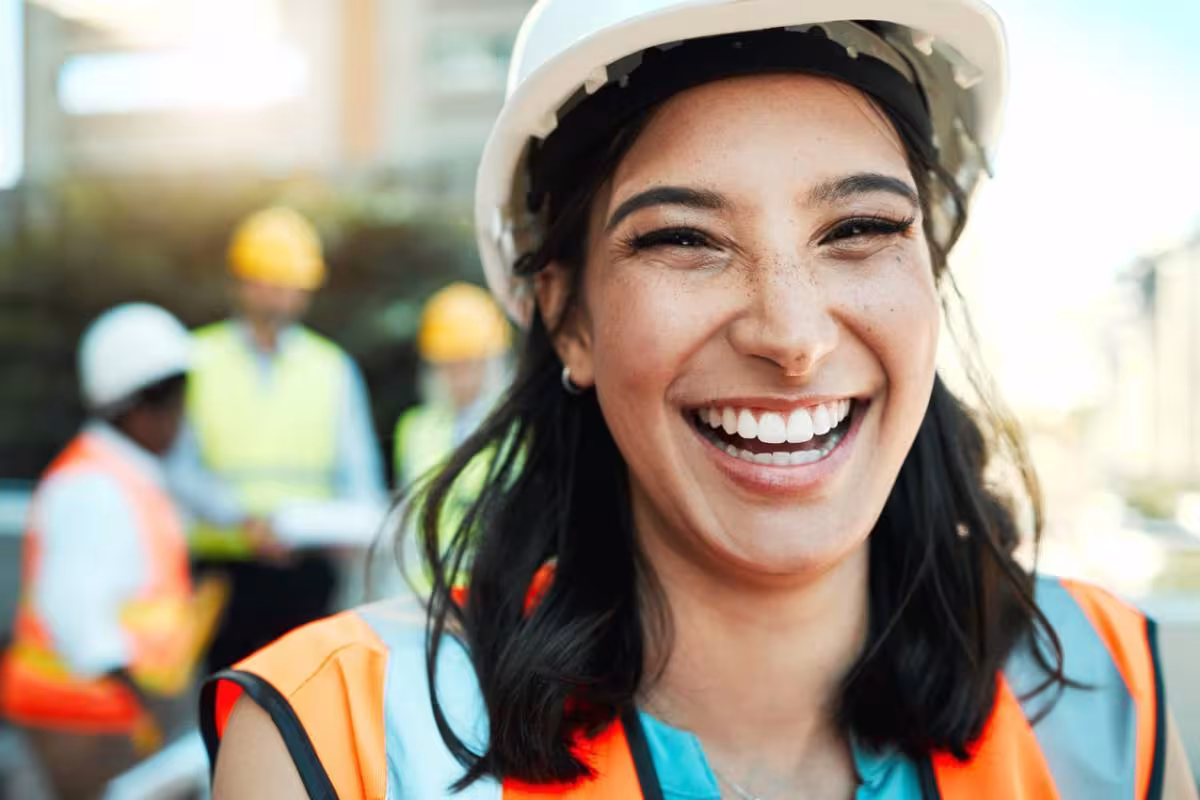 Femme portant un casque et un gilet de sécurité souriant sur un chantier.
