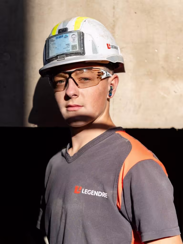 Jeune ouvrier du BTP portant un casque de sécurité et des lunettes de protection.