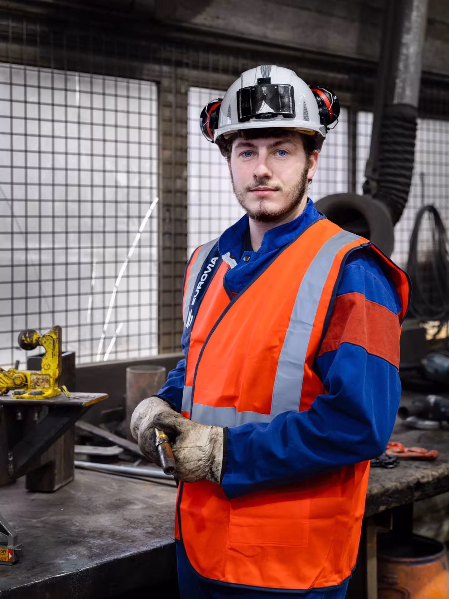 Ouvrier équipé d’un casque et d’un gilet de sécurité dans un atelier industriel.